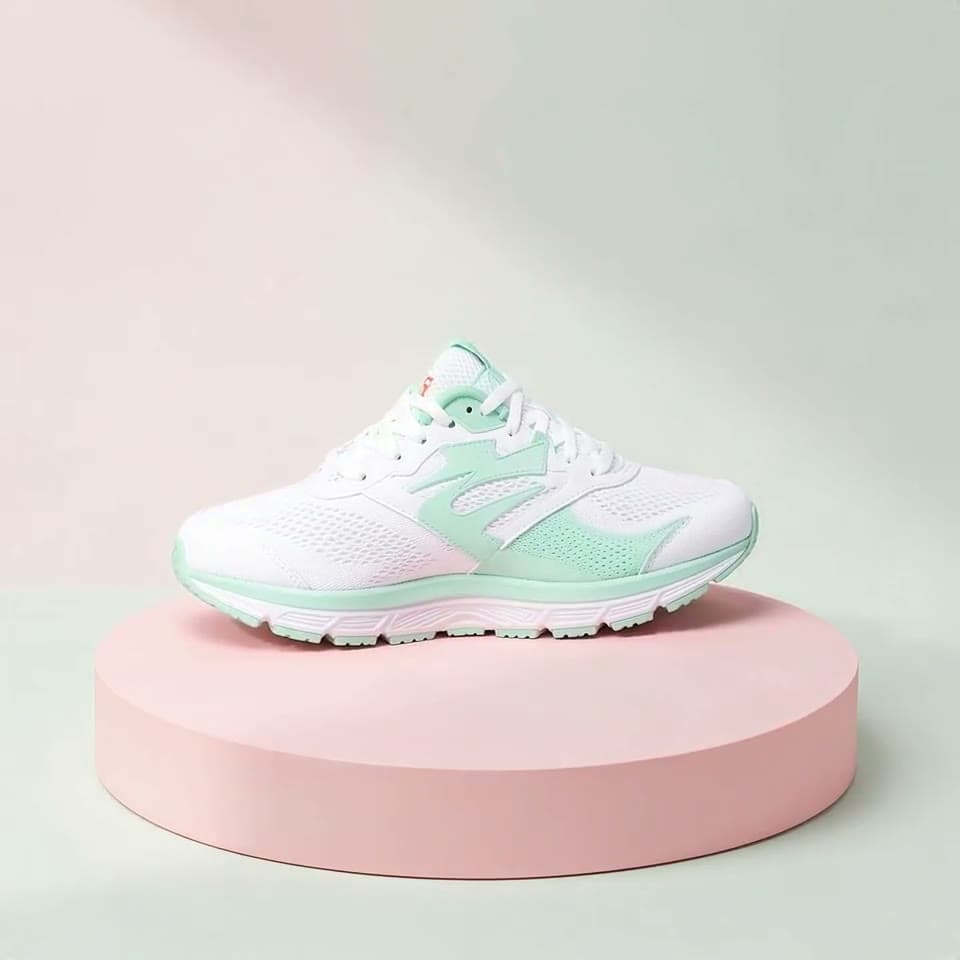 A white and mint sneaker turns slowly on a pink podium as soft light sweeps across it