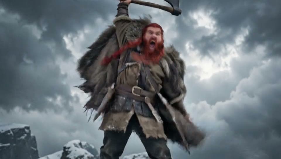 A viking with a braided red beard on a snowy cliff raises his axe and roars as snow blows past