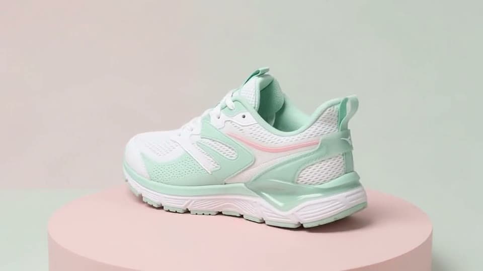 A white and mint sneaker turns a full circle on a pink podium as soft studio light sweeps across it