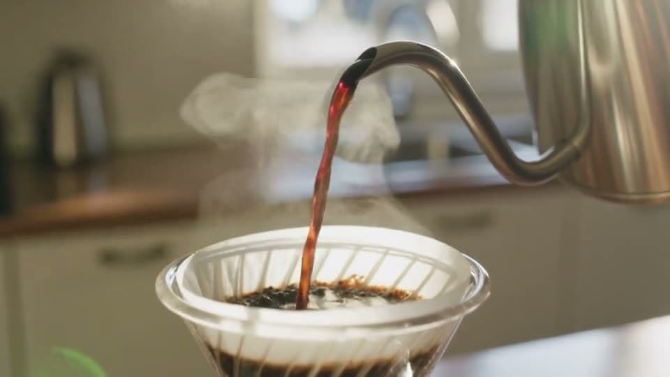 Hot coffee poured from a gooseneck kettle into a pour-over filter in slow motion
