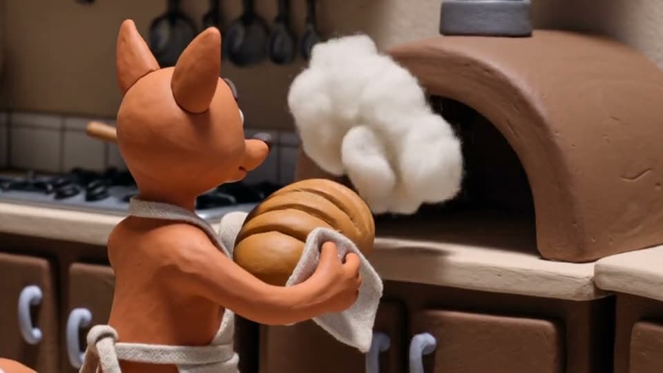A clay fox in an apron pulls bread from a clay oven and smiles